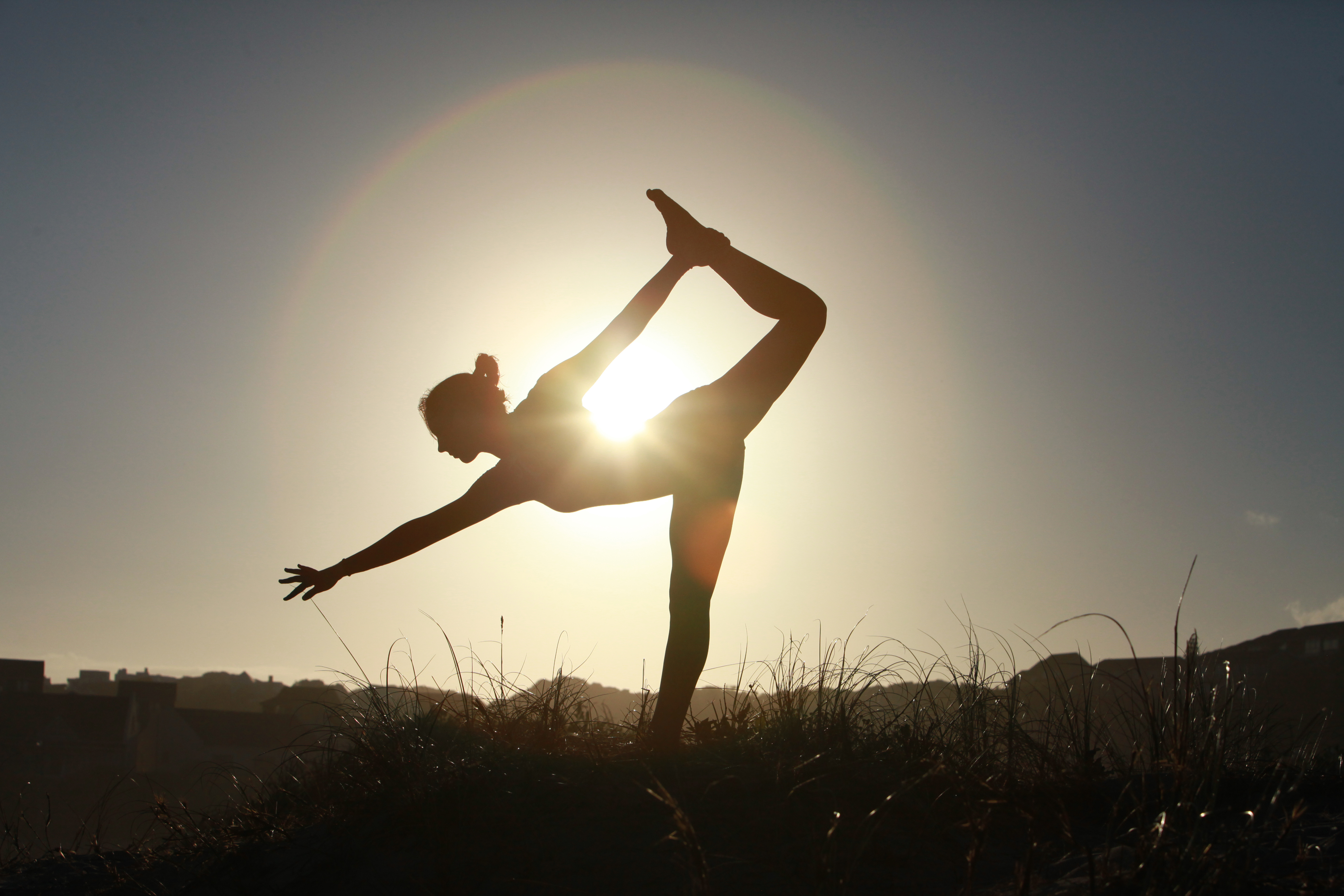 Silhouette of acrobatic teen gymnast balancing with the sun behind her