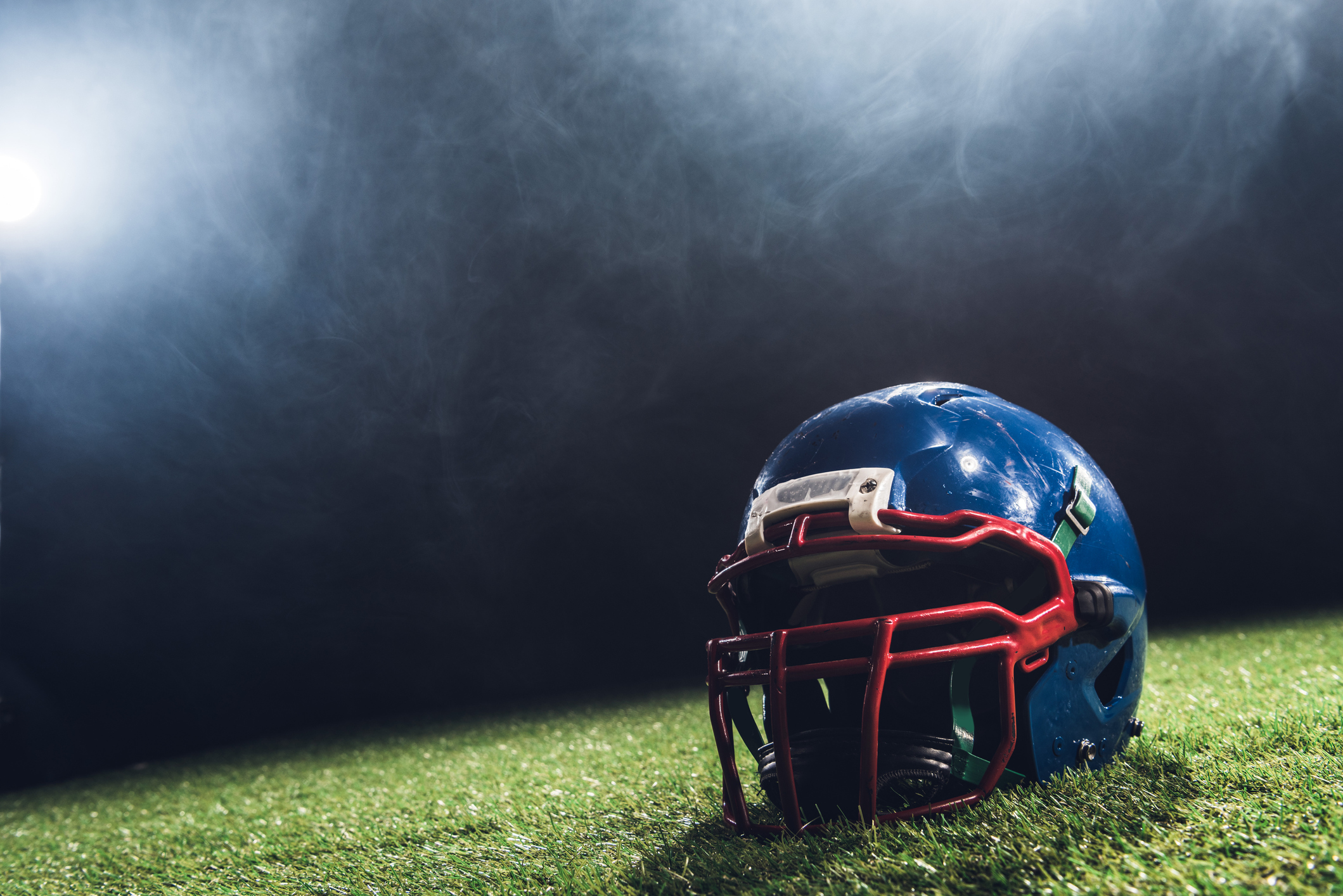 close-up shot of american football helmet on green grass with white smoke above