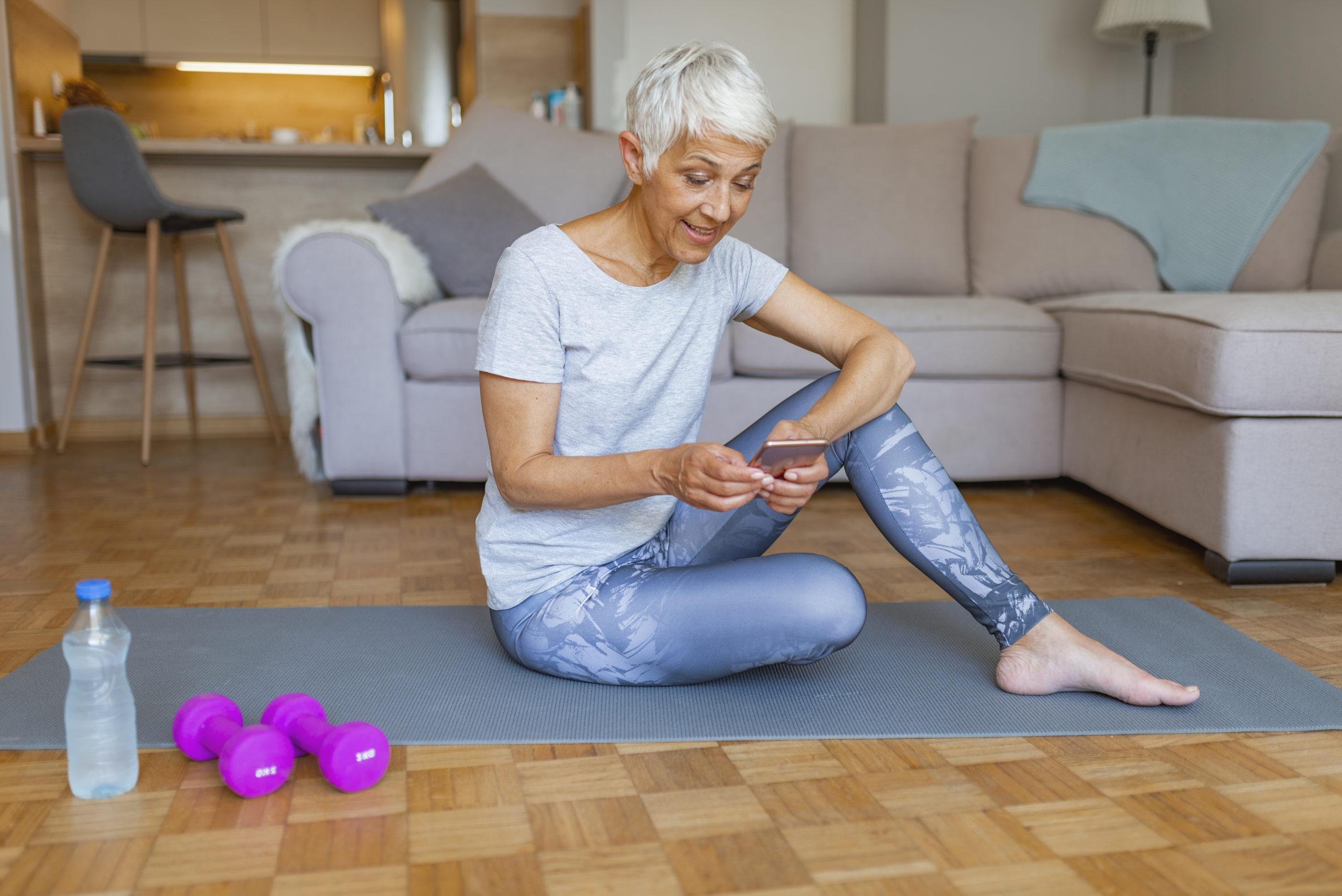 Older woman uses smartphone on yoga mat