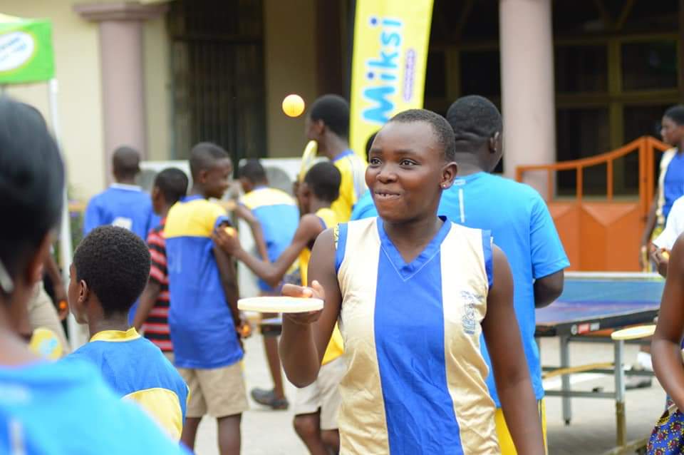 Young woman smiles and bounces a ping pong ball with a paddle.